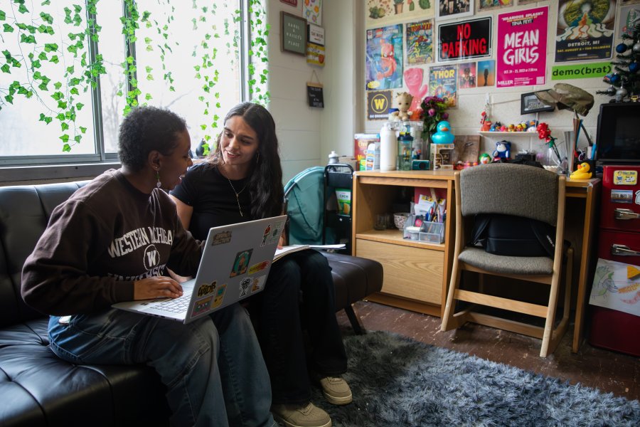 Two students sit on a futon to study in their decorated residence hall room.