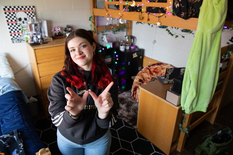 A WMU student poses in their decorated residence hall room making a W sign with their hands.