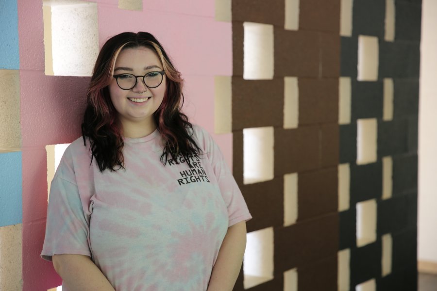 A WMU student wearing a tie-dye t-shirt poses in front of a blue, pink, brown, and black painted wall.