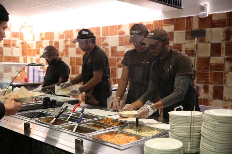 Four students in WMU Dining uniforms dishing up plates of food for a customer at Cilantro's in the Valley Dining Center.