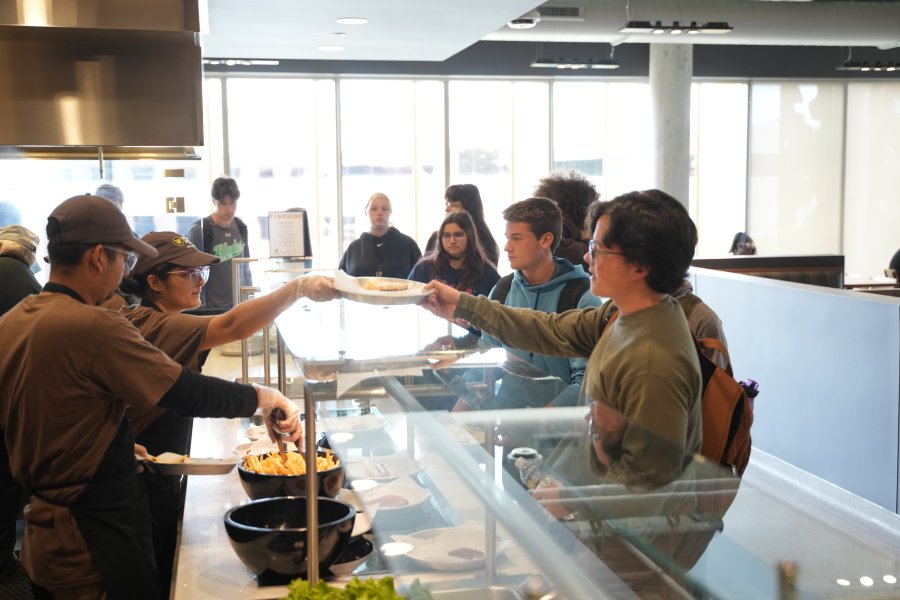 Two WMU Dining student employees handing a plate of food to a student in line.
