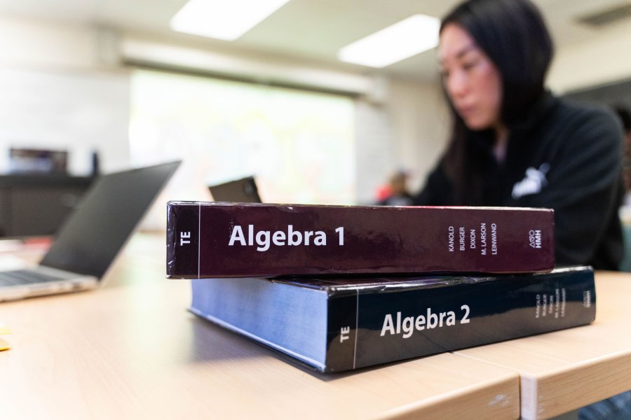 Two Algebra books stacked on top of each sitting on a table in front of a student.