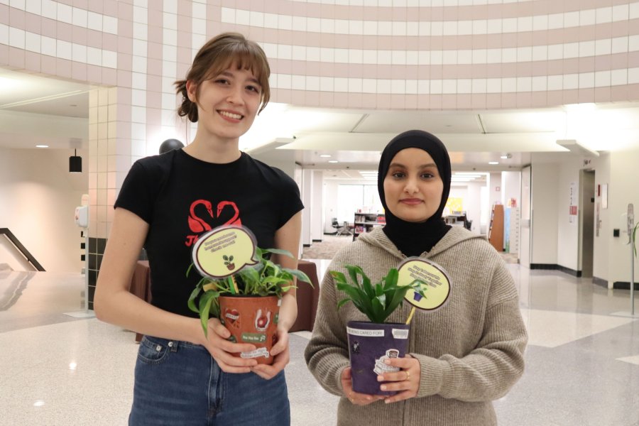 Two students holding small plants that can be checked out at Waldo Library to keep them company during study sessions.
