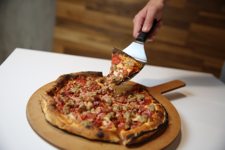 A pizza with meat toppings sitting on a wooden serving platter.