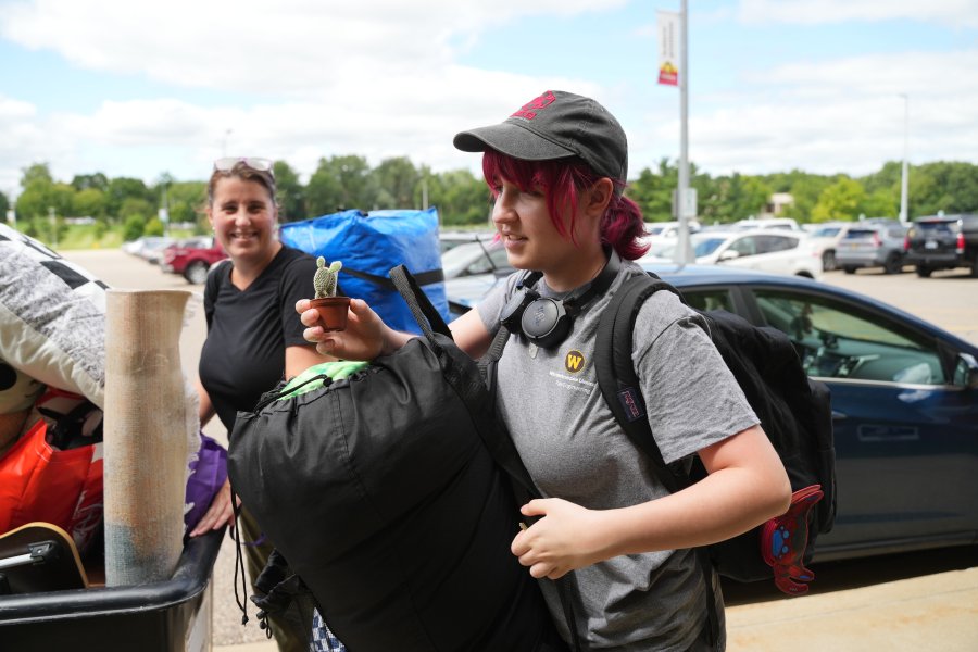 A WMU engineering student carries a house plant and a large bag into their residence hall on move-in day.