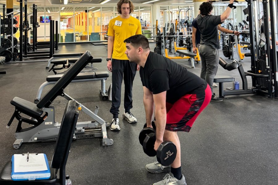 White, male personal trainer working with a white, male participant who is doing rows holding 35 pound dumbells and doing a good morning 