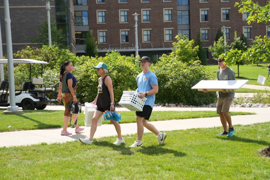 A family carries boxes of personal belongings outside a brick residence hall.