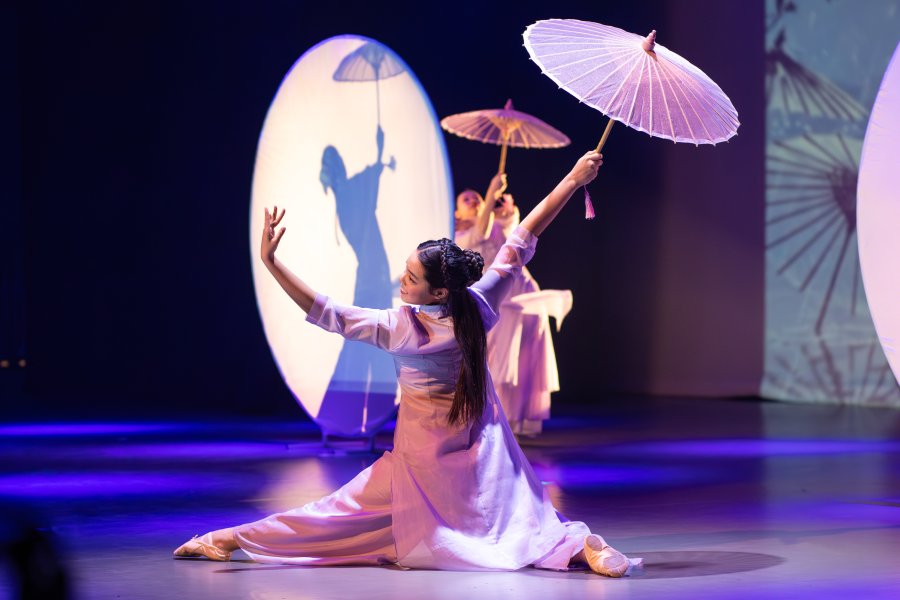 A performer on stage at the 2025 Spring Gala. She holds an Asian fan and dances with the spotlight and shadow.