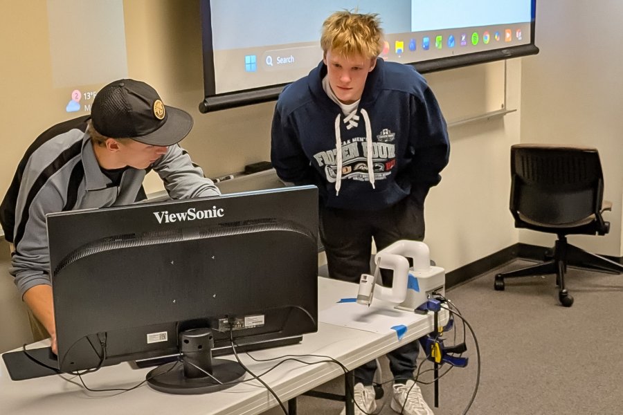 Torrey Cookman shows fellow student how to operate his Cobot