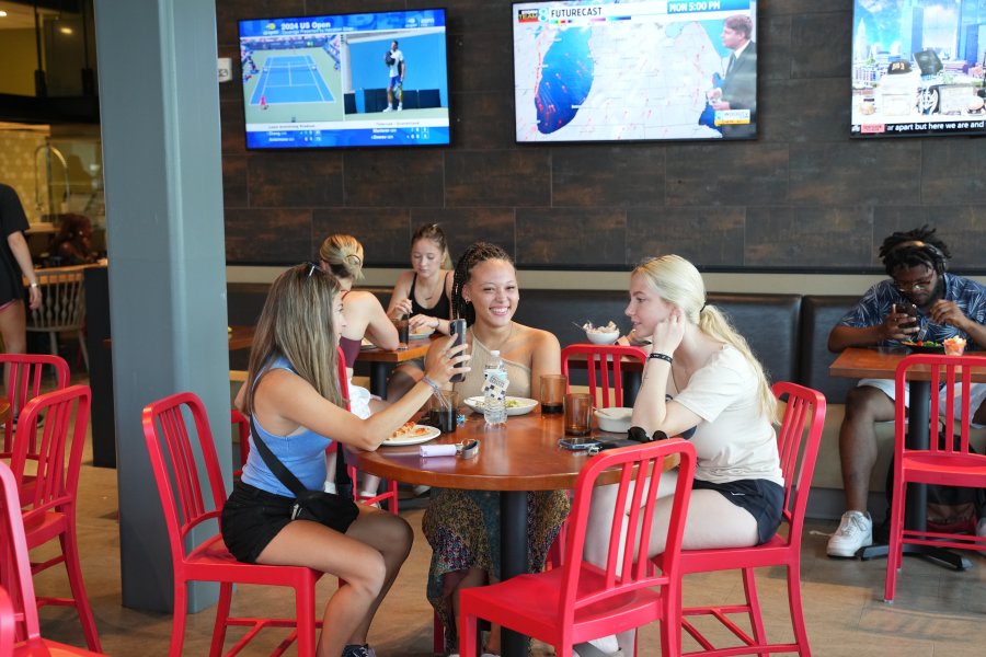 Three students sit at a table with red chairs in the Valley Dining Center.