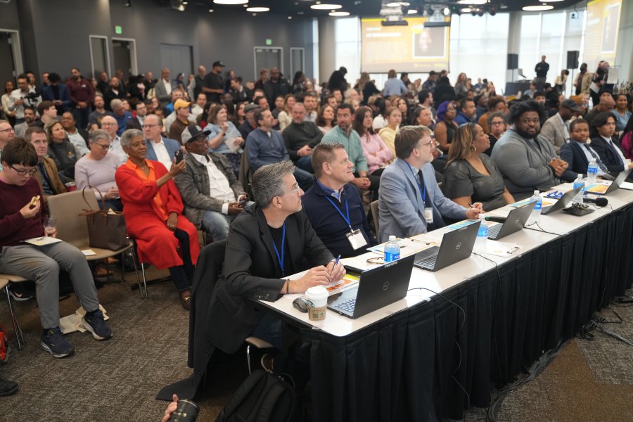 A panel of judges sits at a table in front of an audience at a pitch competition.