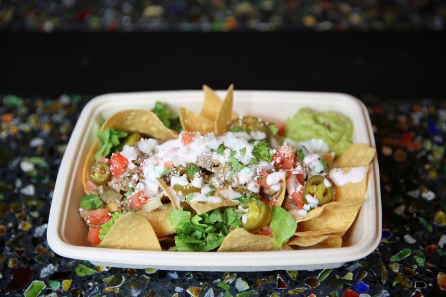 A carryout bowl of nachos topped with cheese, salsa, and guacamole sitting on a multicolored countertop.