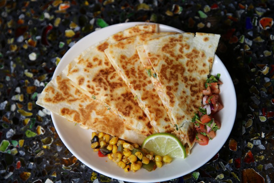 A plated quesadilla with pico de gallo and a lime wedge sitting on a multicolored countertop.