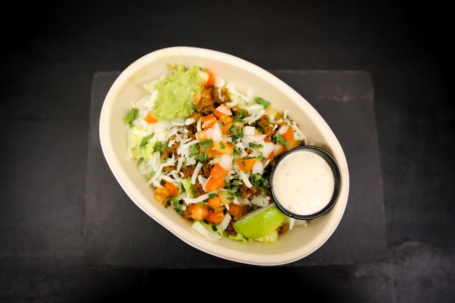 A bowl of freshly-made taco salad with a side of sour cream sitting on a dark countertop.