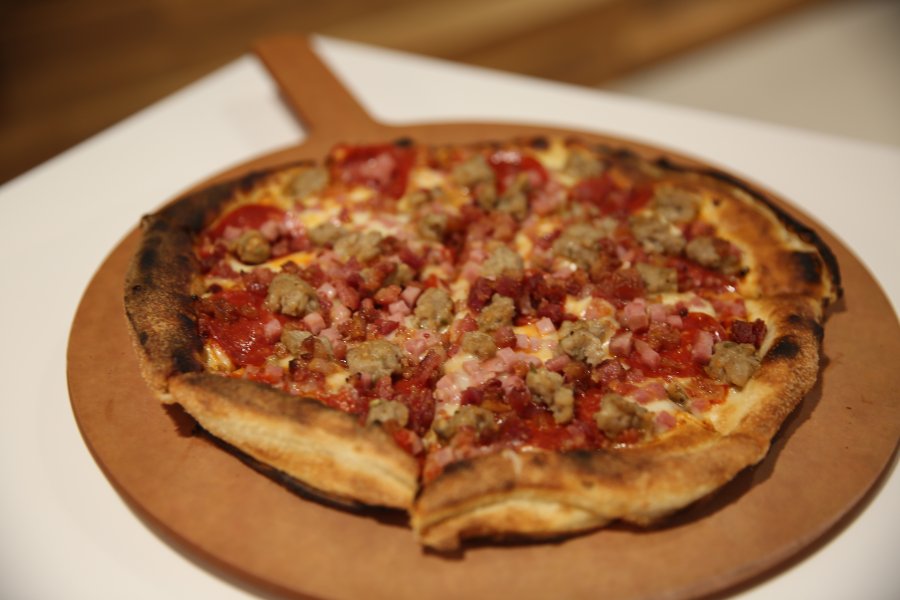 A My Pie meat lovers pizza on a circular wooden serving tray.