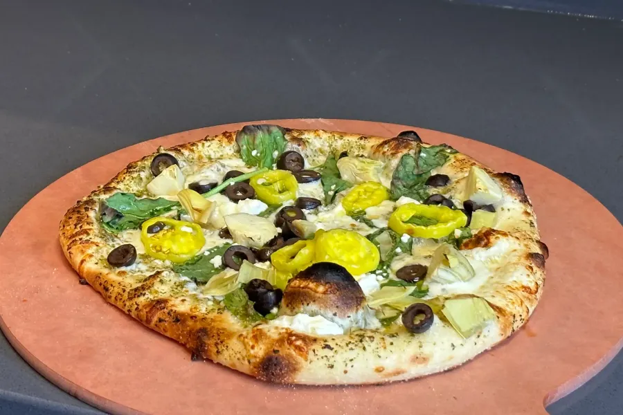 A greek pizza from My Pie sitting on a red pizza stone.