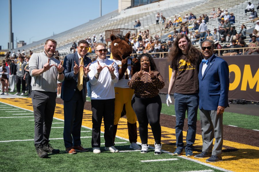 WMU's president stands on the football field with students and athletics staff.