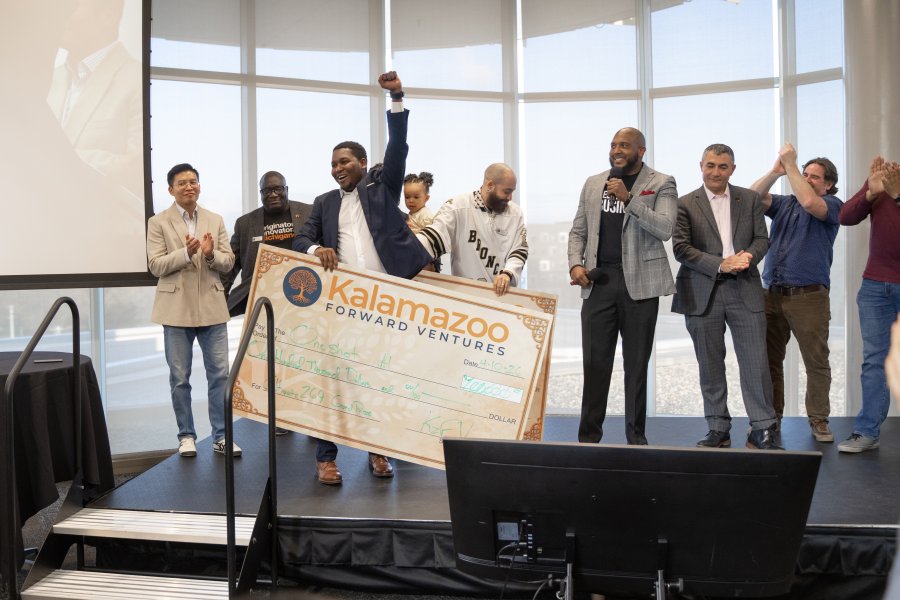 Samuel Marseille stands on stage with Cultivate 269 stakeholders while holding a giant $100,000 check.