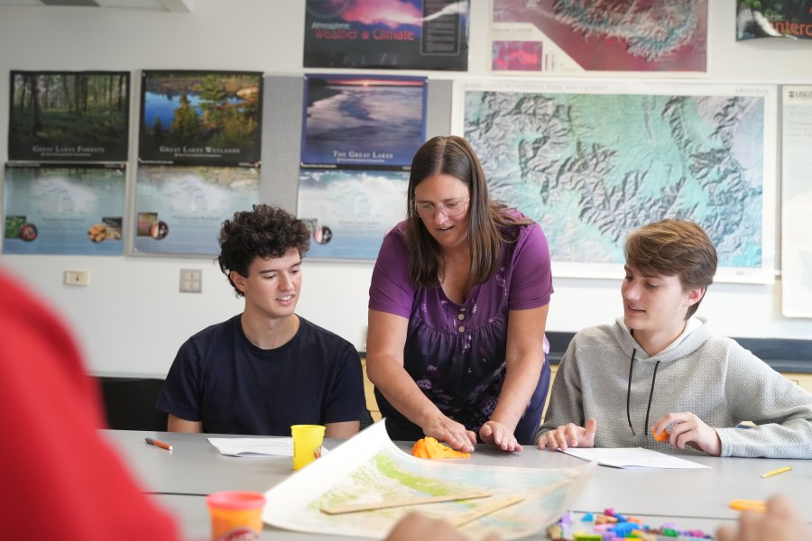 A professor and a group of students speak at a table.