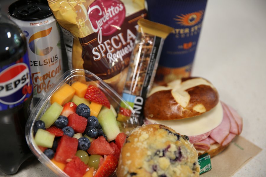 Close up of Campus Cafe offerings including assorted fresh cut fruit, baked muffins, prepared sandwiches as well as bottled beverages, snacks and Water Street Coffee.