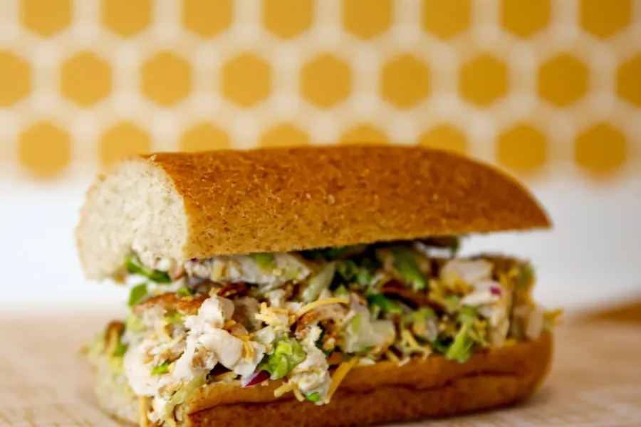 A half sub, chicken salad-style sandwich on bread with an orange tile background.