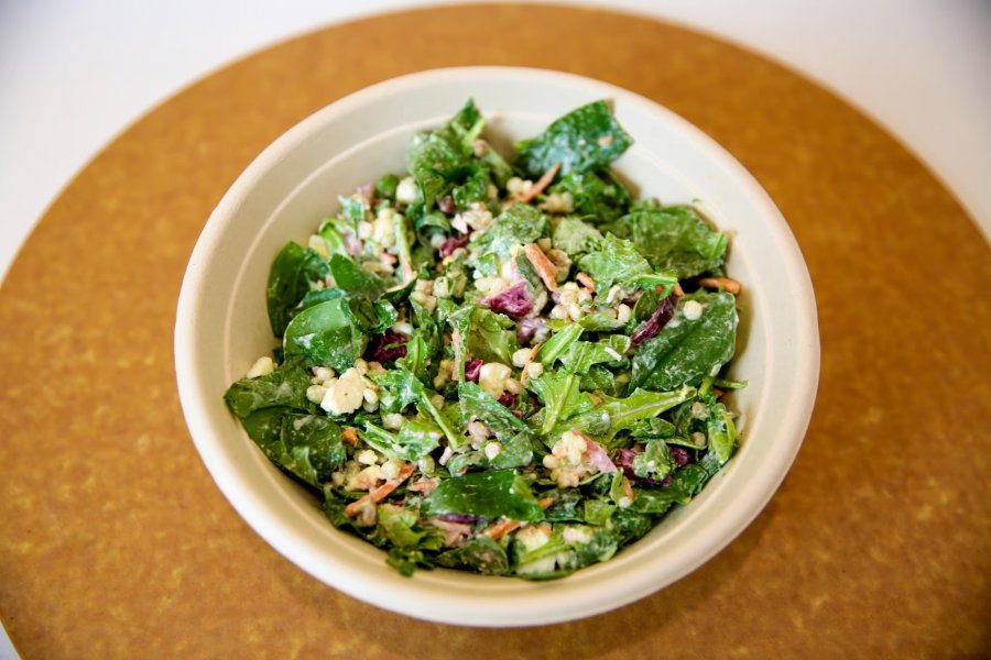 A freshly-made salad with couscous, egg, onions and greens in a take out bowl.