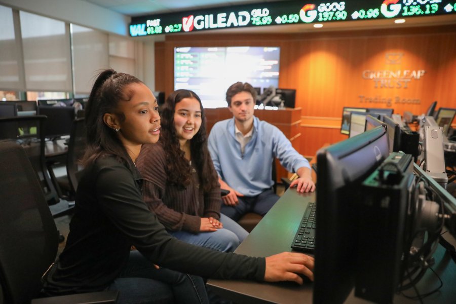 Three students at a Greenleaf room computer discussing assignments