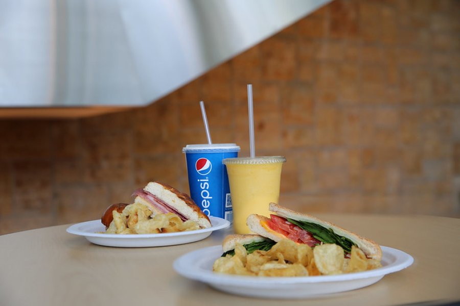 Two sandwiches, a Pepsi fountain beverage and a smoothie are sitting on a table in the seating area of a cafe. 