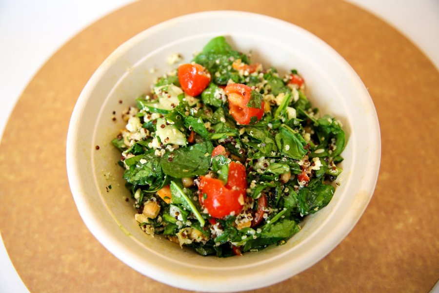 A freshly-made grain bowl with quinoa, spinach, tomatoes, and feta in a take out bowl.