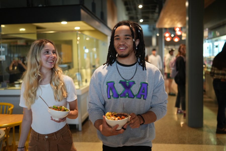Two students walking to a table with stir-fry bowls from Pacific Plate at the Valley Dining Center..