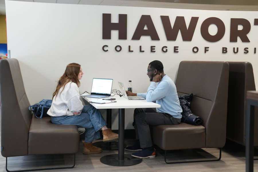 Two students conversing with laptops and a beverage from Schneider Cafe. 