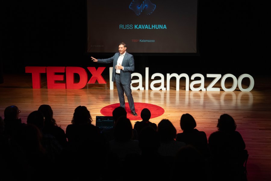 Russ Kavalhuna in front of the TedxKalamazoo sign, speaking to a crowd