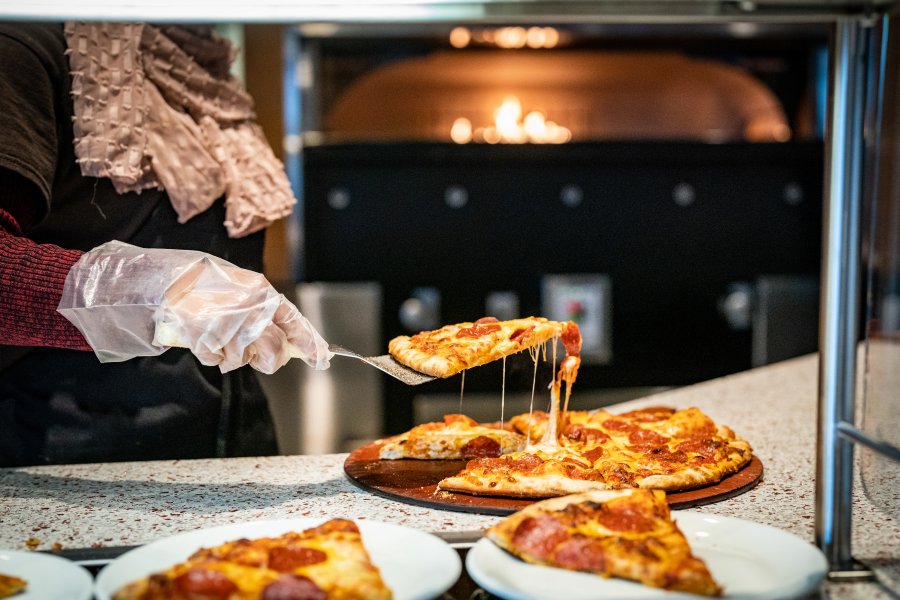 Student employee scooping up a piece of pepperoni pizza at Pastaria inside the Valley Dining Center.