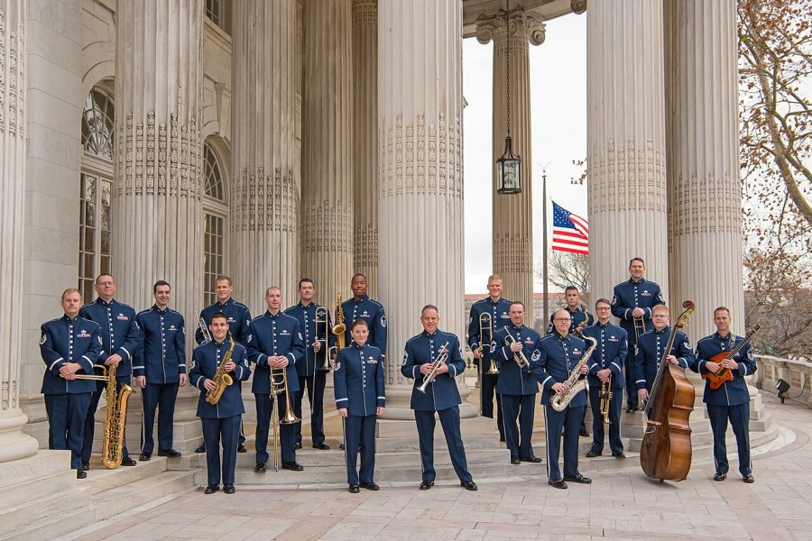 A jazz ensemble in military dress stands in front of a building with large marble columns.