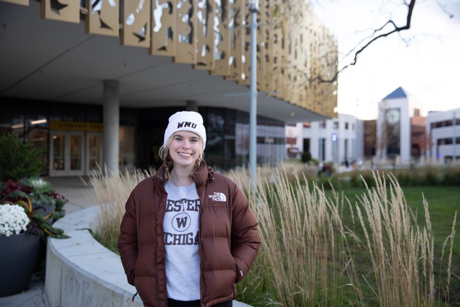 Student wearing WMU hat and sweatshirt smiles outside of the Student Center.