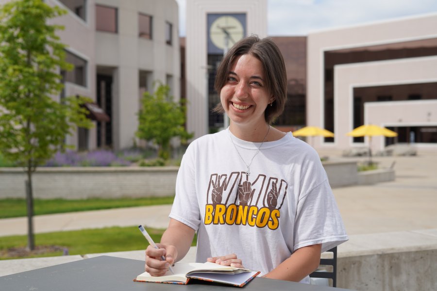 WMU student, Audrey, sits at a table in front of Waldo Library with her journal