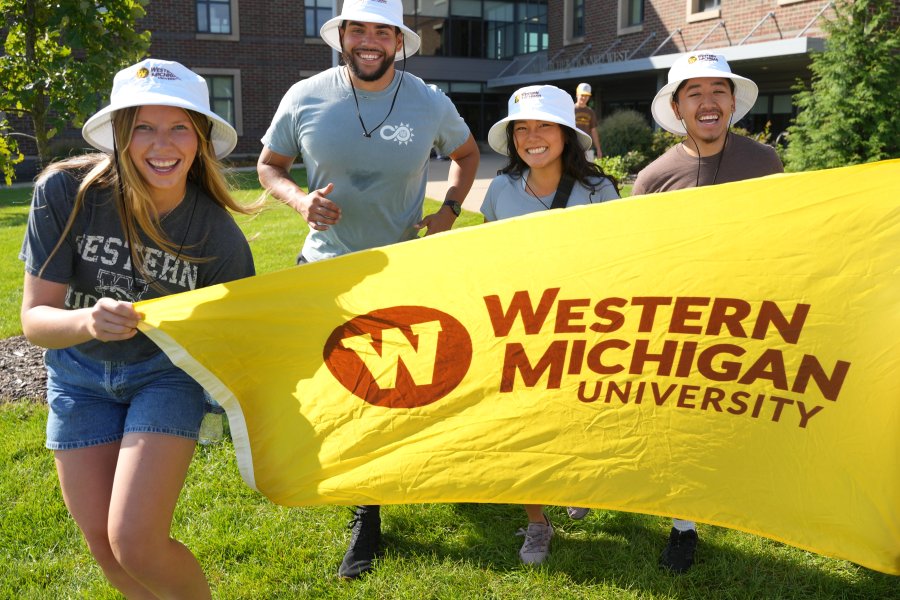 Students run with a yellow Western flag in front of a residence hall.