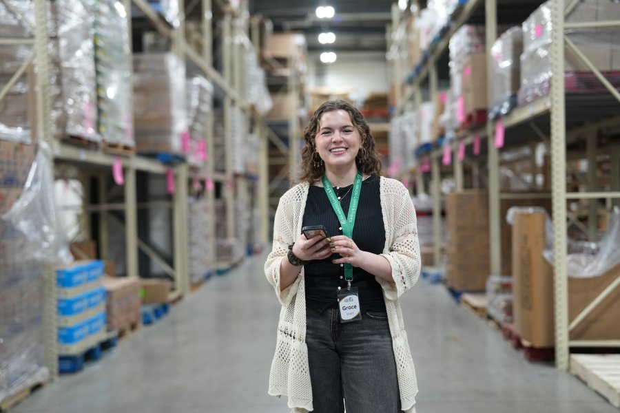 Grace Mulock holds up her cell phone in the aisle of a warehouse.