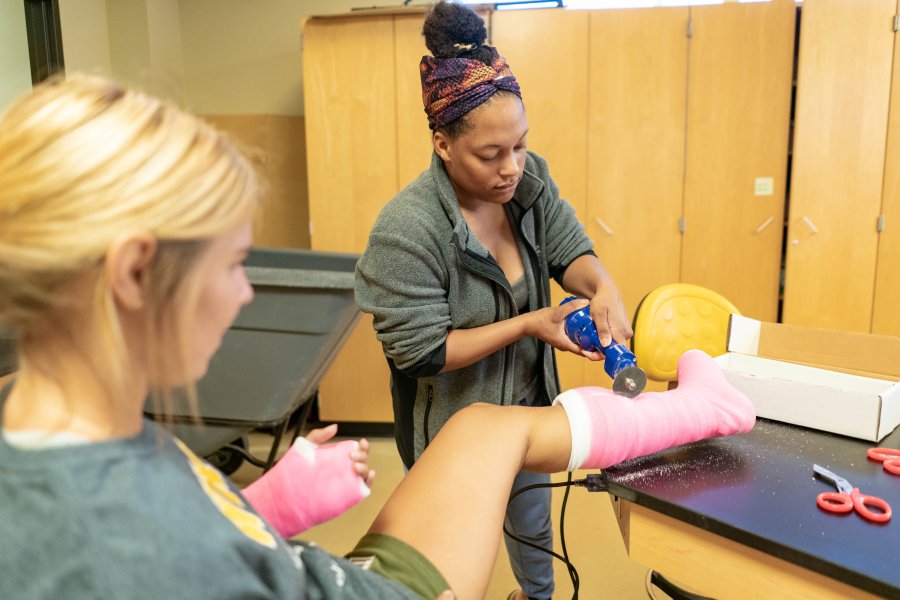 Two female PA students practice cast removal in a lab.