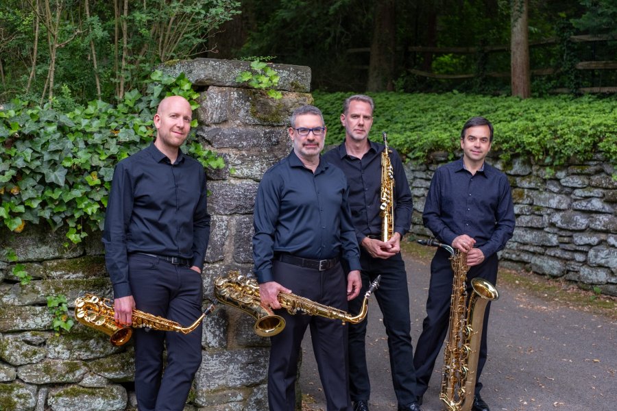 Four men in dark-colored clothing holding saxophones.