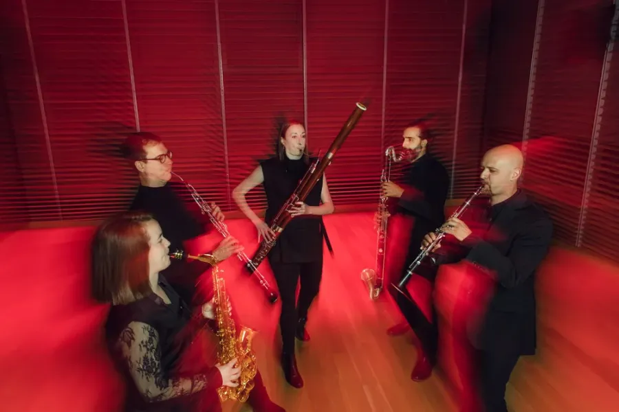 A slightly blurred action shot of five woodwind players performing on a red-lit stage.