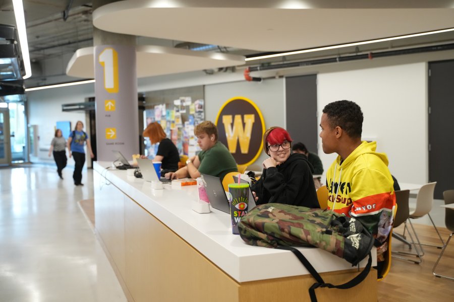 Students sitting at a counter in front of ReFresh Market with a variety of beverages and their laptops on the first floor of the Student Center.