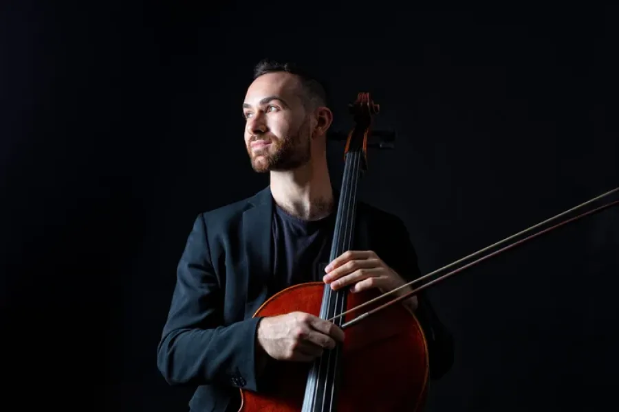 A man in a dark suit holding a cello. 
