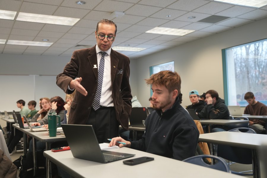 A professor speaks to students at a table in a classroom.