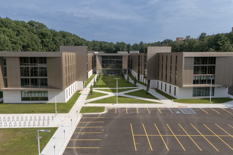A drone shot of a modern, H-shaped residence hall with a brown exterior and large windows.