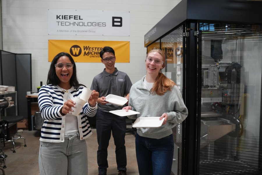 Three graduate students standing with paper products. 