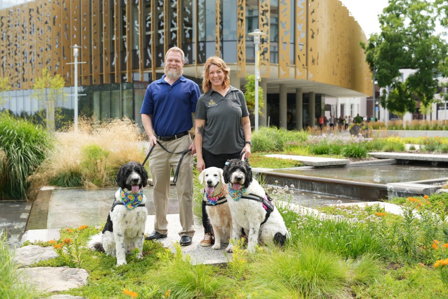 Angela Moe and her husband pose in front of CHHS with their therapy dogs