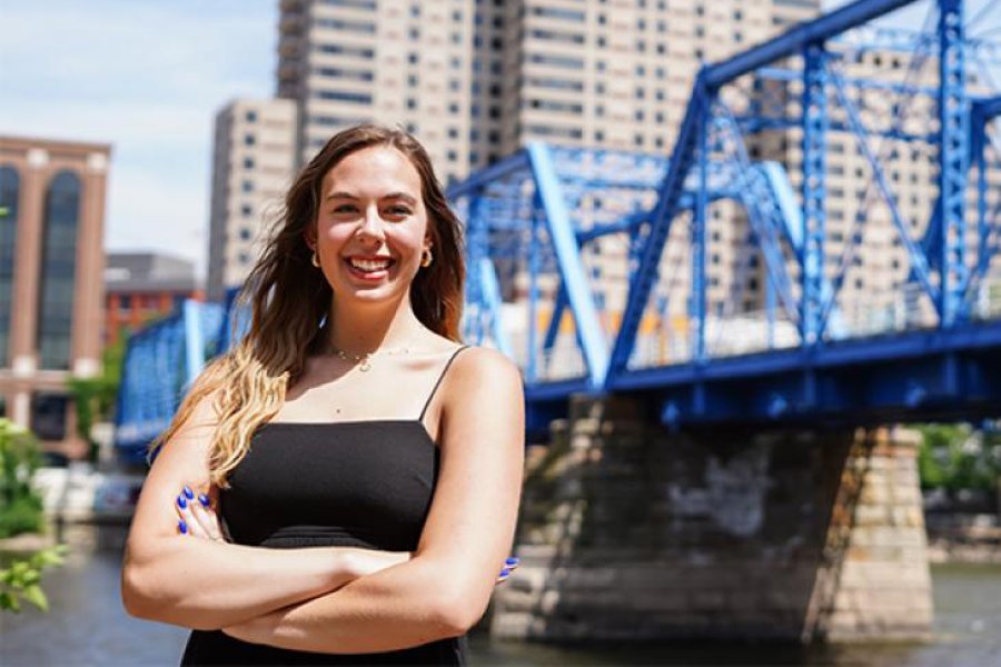 A student standing in front of the Grand Rapids bridge
