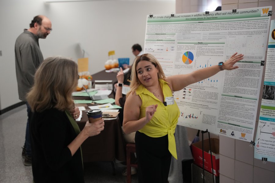 a female student talks with an adult woman while pointing at a poster of research findings