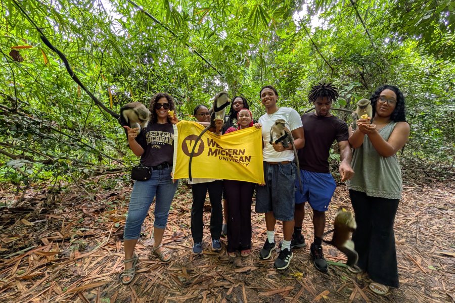 WMU study abroad students stand in the jungle with monkeys while holding WMU flag. 